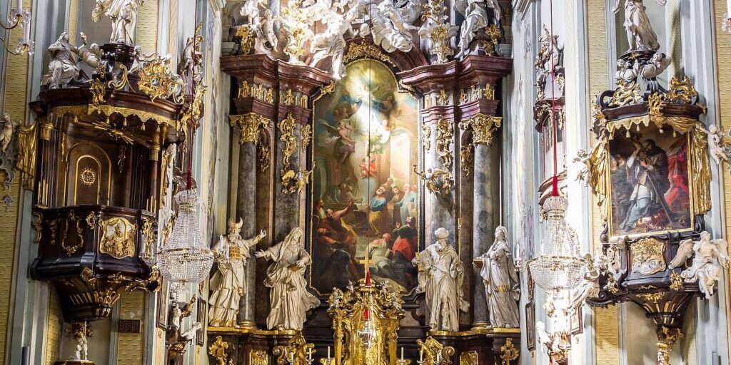 Baroque church interior with a red carpeted aisle leading to a gilded altar beneath painted ceiling frescoes.