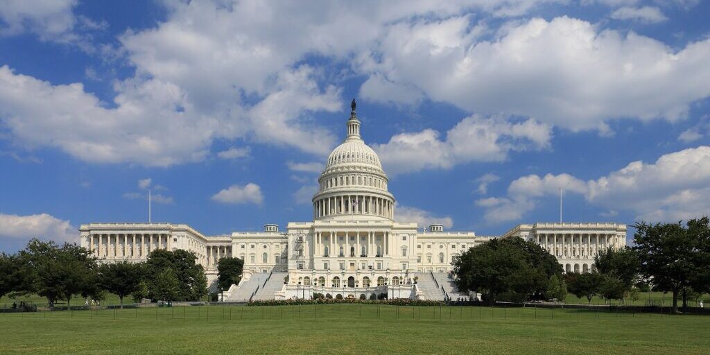 The U.S. Capitol building viewed from the west, its white dome and columned facade under a blue, partly cloudy sky