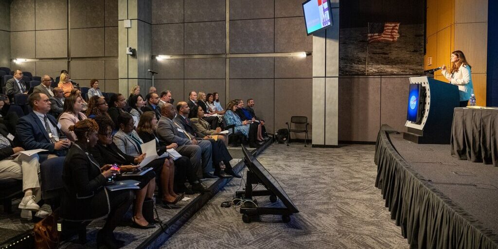 Audience seated facing a speaker at a federal government procurement event
