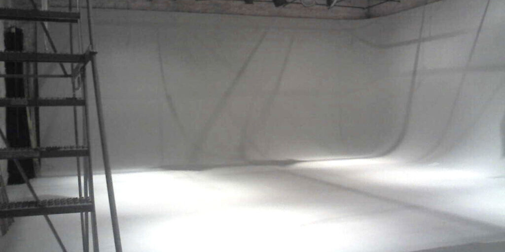 Interior of a sound stage with suspended lighting rigs and an open floor